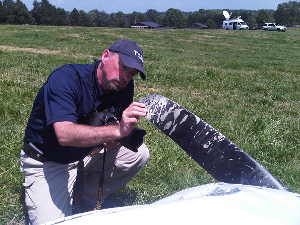 A TSB investigator examining the propeller of the crashed aircraft