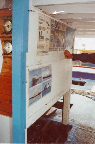 Photo of the lifejacket locker in engine casing with door in closed position showing LIFEJACKETS sign (arrow) and posters on door