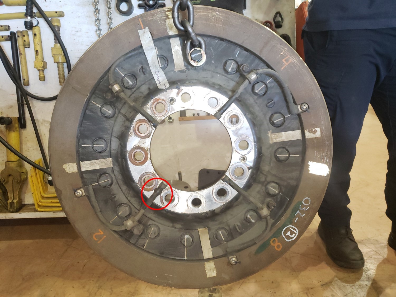 R12 wheel on LRV 1133 with reported wheel hub crack identified (tape and arrow) and 1 jacking screw obscured by a grounding cable (circle) (Source: TSB)