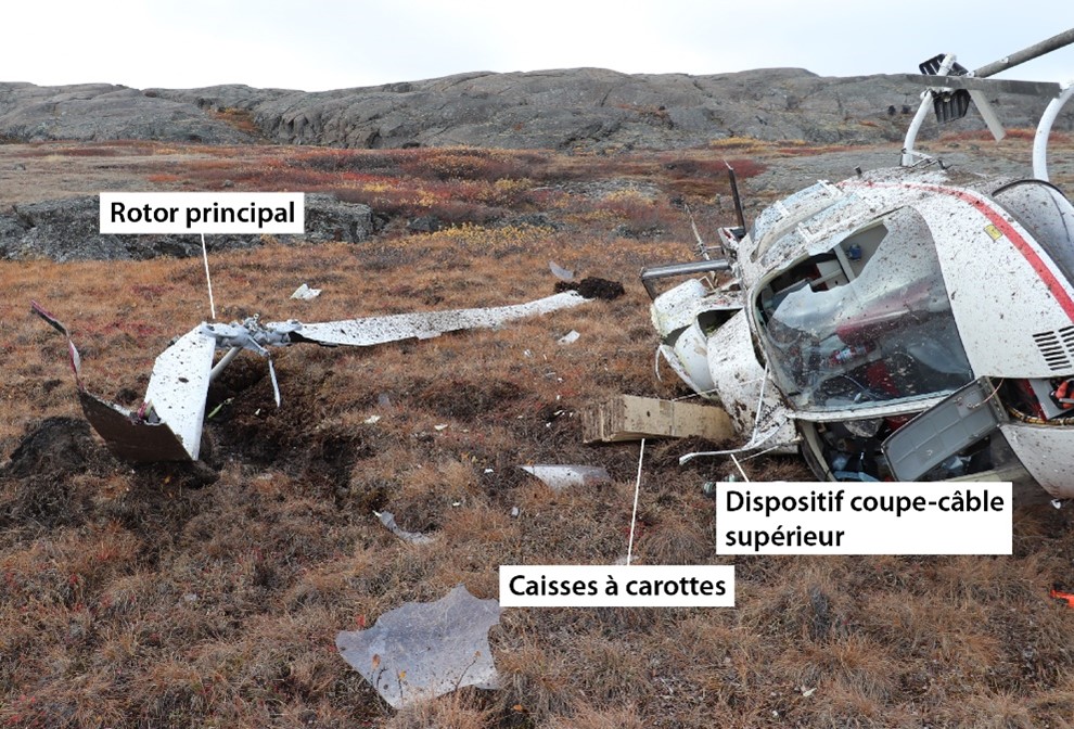 Photo de l’épave montrant l’hélicoptère sur son côté droit, le rotor principal et les caisses à carottes (Source : Gendarmerie royale du Canada)