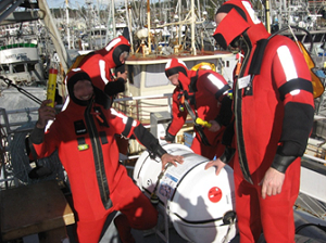 Journée d'exercice de l'industrie. Quatre pêcheurs vêtus d'une combinaison d'immersion se réunissent près du radeau de sauvetage, à bord de leur bateau attaché au quai du port de Comox (Colombie-Britannique)